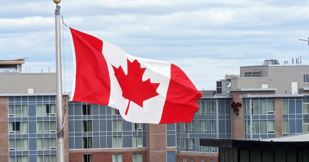 Canadian flag waving in the wind in front of modern urban buildings.